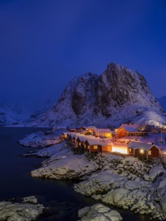 Rorbuer huts of Hamnoy at the fjord at dusk, snowy mountains in the background, Hamnøy, Reine,