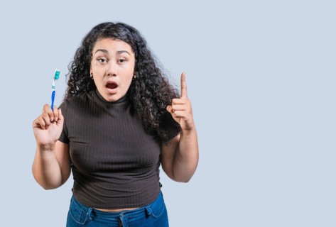 Surprised woman holding toothbrush pointing up. Amazed girl holding toothbrush and pointing up