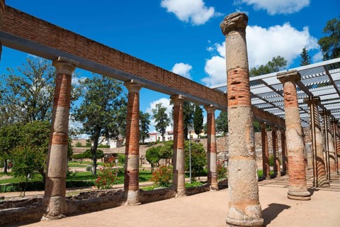 Ancient row of columns in a ruined site, surrounded by nature and under a clear sky, Mérida,