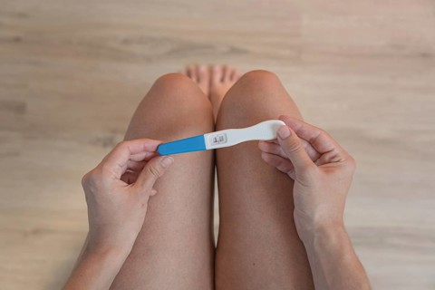 A person holds a positive pregnancy test above their knees, symbolic image of new life, wooden