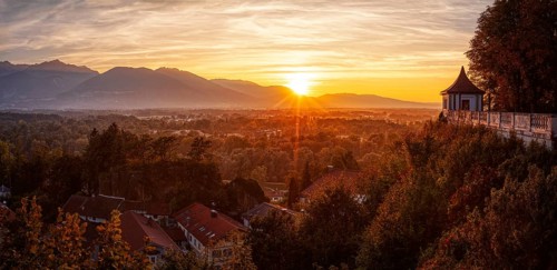 A picturesque sunset over an autumnal landscape with mountains and a building in the foreground,