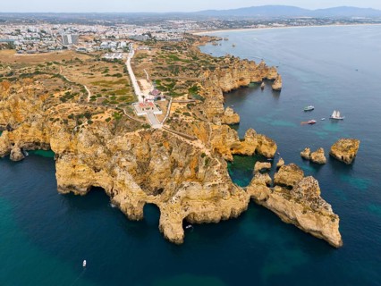 Steep cliffs and rocky coastline with blue sea, beyond a town and distant mountains, aerial view,