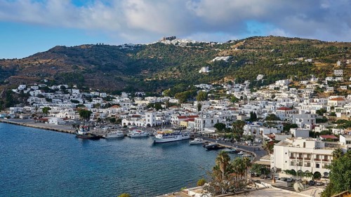 Panoramic view of a coastal town on a Greek island with white buildings and hills stretching to the