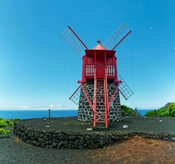 Traditional red windmill Moinho de São João made of volcanic stone in front of a clear blue sky,