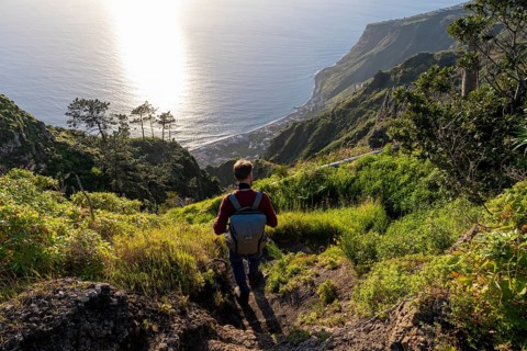 Young man looking out to sea on cliff, evening mood, green coastal landscape on cliff, sea and
