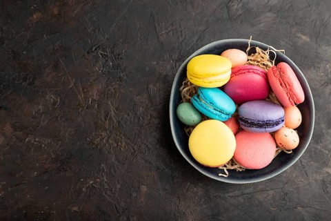 Multicolored macaroons and chocolate eggs in ceramic bowl on black concrete background. top view,