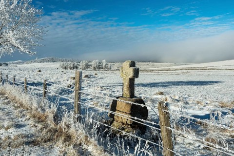 Aubrac plateau in winter. Stone cross at the side of a path. Lozere department. Occitanie. France