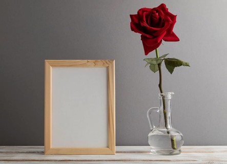 White wooden frame mockup with red rose in glass on gray paper background. Blank, vertical