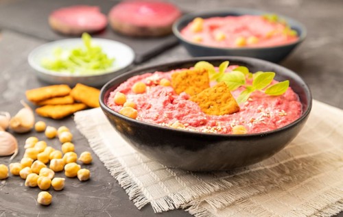 Hummus with beet and microgreen basil sprouts in ceramic bowl on a black concrete background and