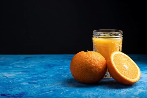 Glass of orange juice on a black and blue background. Hard light, contrast. Side view, copy space