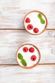 Yogurt with raspberry in clay cups on white wooden background. top view, flat lay, close up