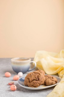 Homemade oatmeal cookies with a cup of cocoa and a yellow textile on a gray and orange background.
