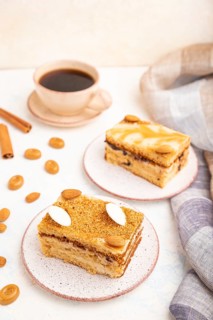 Honey cake with milk cream, caramel, almonds and a cup of coffee on a white concrete background and