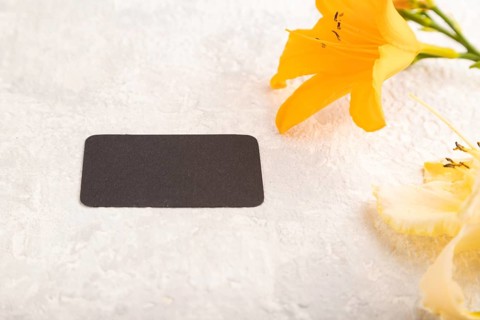 Black paper business card mockup with orange day-lily flower on gray concrete background. Blank,