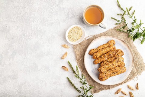 Crumble cookies with seasme and almonds on ceramic plate with cup of green tea and linen textile on