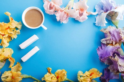 Purple, pink, yellow iris flowers and a cup of coffee on pastel blue background. Morninig, spring,