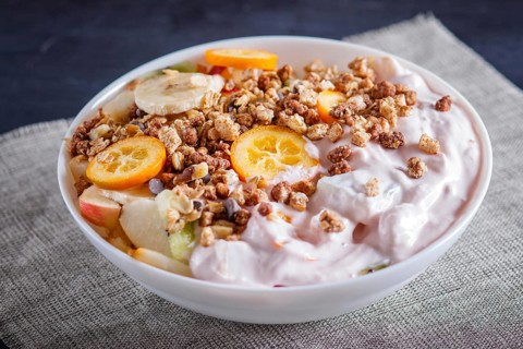 Vegetarian salad of bananas, apples, pears, kumquats, kiwi with granola and yogurt on black woodem