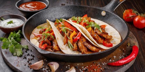 A plate and prying pan of fajitas with three tacos and tortillas and a bowl of salsa sauce, AI