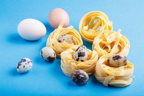 Raw uncooked tagliatelle pasta with quail eggs on a blue pastel background. side view, close up