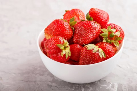 Fresh red strawberry in white bowl on gray concrete background. side view, close up, selective