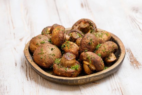 A variety of freshly picked mushrooms is beautifully arranged on a rustic wooden plate, sprinkled