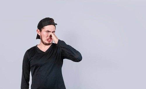 Young man covering nose isolated. Guy with a face of unpleasant odors covering nose