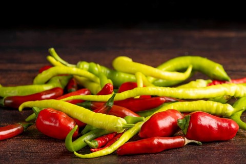 A mixture of green and red peppers lies on a dark wooden surface, food photography