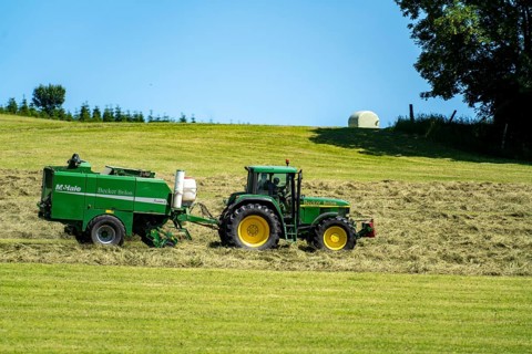 Hay harvest, farmer with agricultural machine, picks up mown hay, which is immediately pressed into