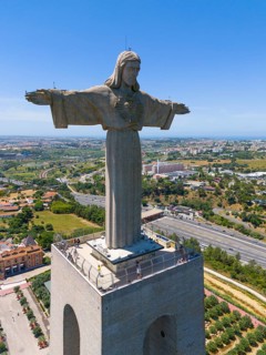 Large statue of Jesus with outstretched arms on a platform, overlooking the cityscape on a clear