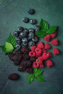 A mix of ripe berries, with leaves scattered on the table, raspberries, blackberries, blueberries,