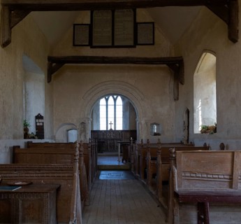 Norman chancel arch and wooden pews inside church of Saint John the Baptist, Wantisden, Suffolk,