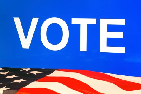 USA flag in front of a blue screen with the inscription VOTE