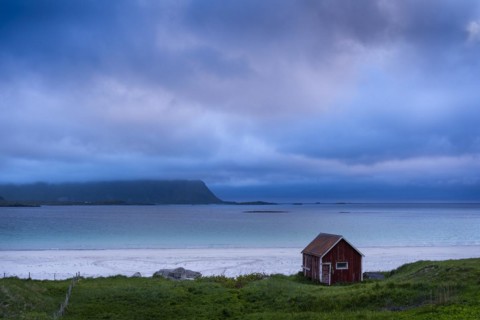 A red wooden hut on the sandy beach of Ramberg (Rambergstranda), sea and mountains. At night at the
