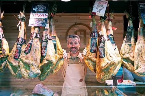Castilian man, 40 years old, between Iberico hams for sale at the Mercado Central, Salamanca,