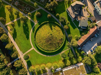 Aerial view of a green Celtic burial mound with circular path surrounded by houses and trees,