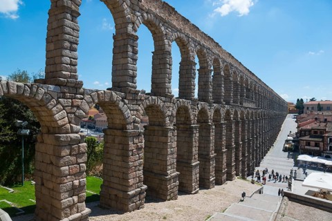Historic aqueduct with stone arches, under a sunny sky with buildings in the background, Aqueduct,