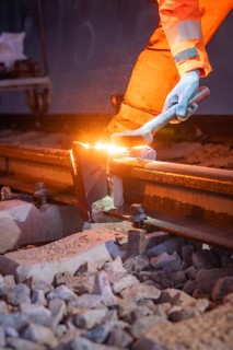 Worker working on rails with sparks, wearing orange work outfit, welding rails, track construction
