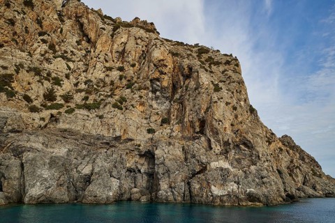 Steep cliff on the shore, light blue sky with few clouds above, boat tour Saria, Saria Island,