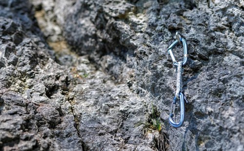 A carabiner hangs from a hook on a rock face. Climbers use the so-called quickdraws to secure