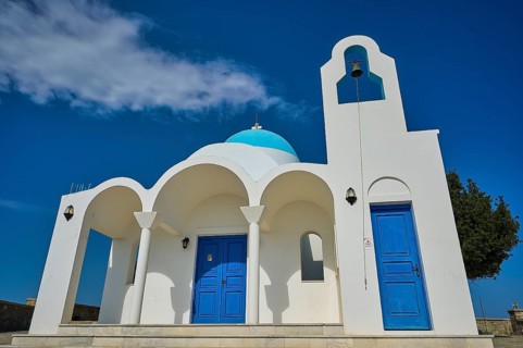 White church with blue doors and a bell against a blue sky, Church of Profitis Ilias, above Nikia,