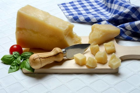 A piece of Parmesan cheese and chopped pieces of cheese on a wooden board