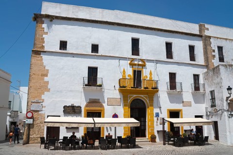 A historic building with a white façade and yellow entrance, including a street café with parasols,
