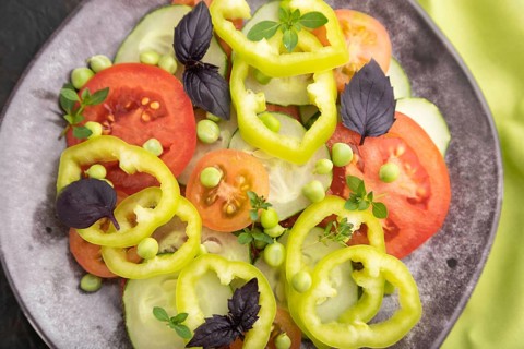 Vegetarian salad from green pea, tomatoes, pepper and basil on a green textile. Top view, close up,