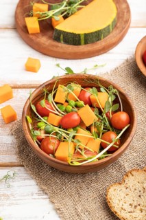 Vegetarian vegetable salad of tomatoes, pumpkin, microgreen pea sprouts on white wooden background