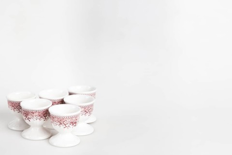 A set of white and red ceramic egg cups with a floral pattern arranged on a light-coloured