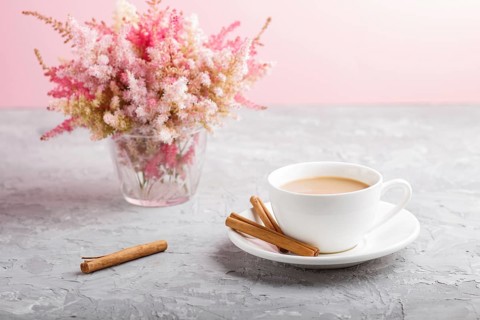 Pink and red astilbe flowers in glass and a cup of coffee on a gray and pink background. Morninig,