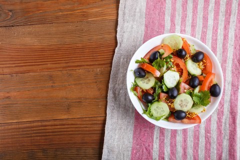 Vegetarian salad of tomatoes, cucumbers, parsley, olives and mustard on linen tablecloth, top view,