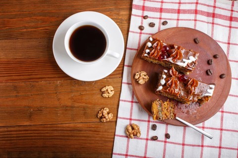 A piece of cake with caramel cream on a wooden kitchen board and a cup of coffee, brown wooden