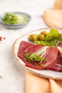 Slices of smoked salted meat with cilantro microgreen on gray concrete background and orange