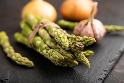 Bunch of fresh green asparagus, garlic, onion on slate board on black concrete background. Side